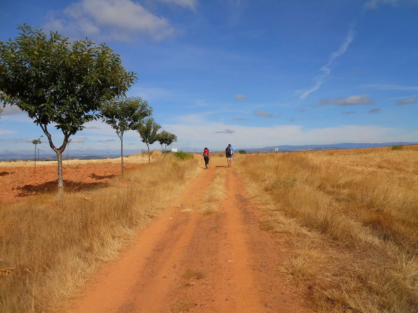 Dos peregrinos caminan por un sendero de tierra roja